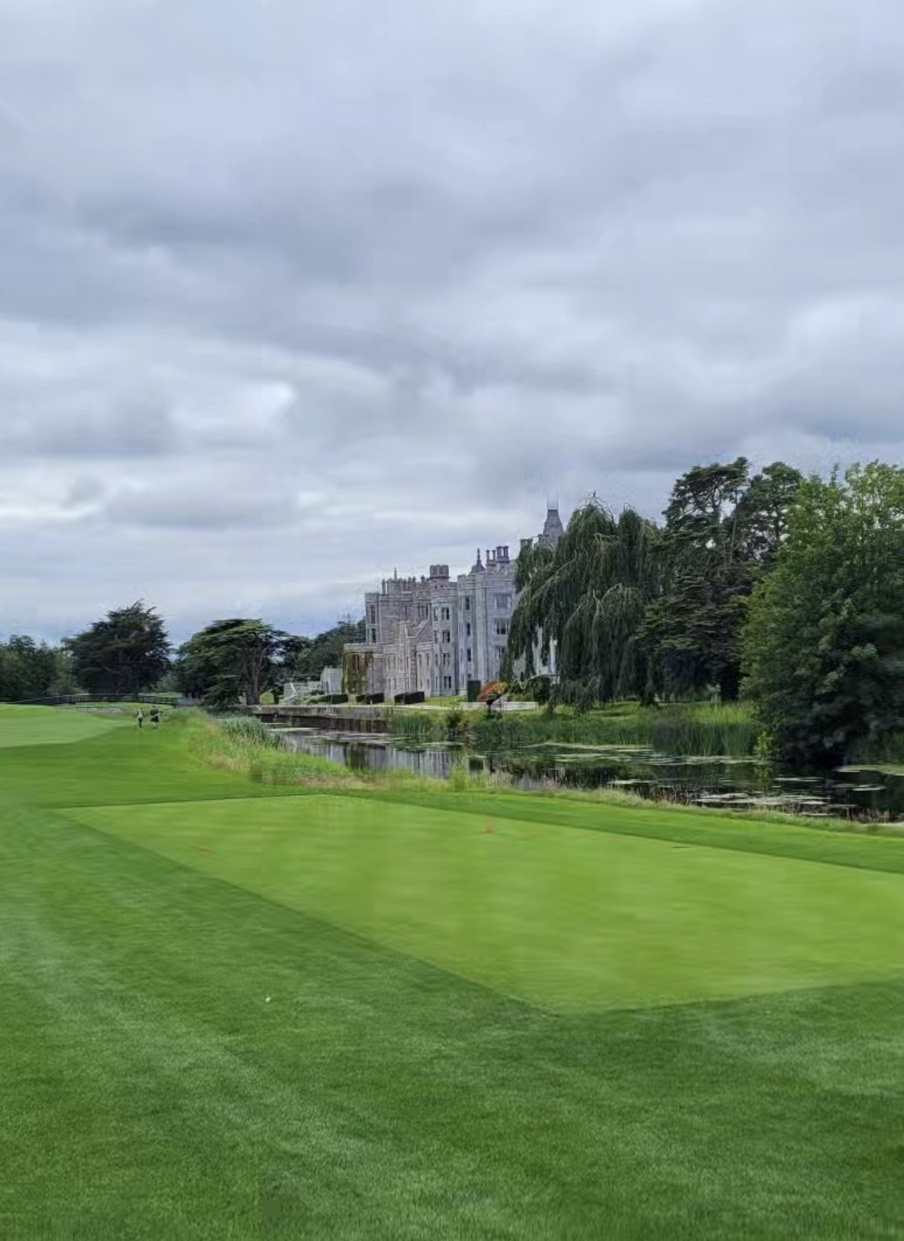 Adare Manor house seen across the river from a manicured fairway under grey skies