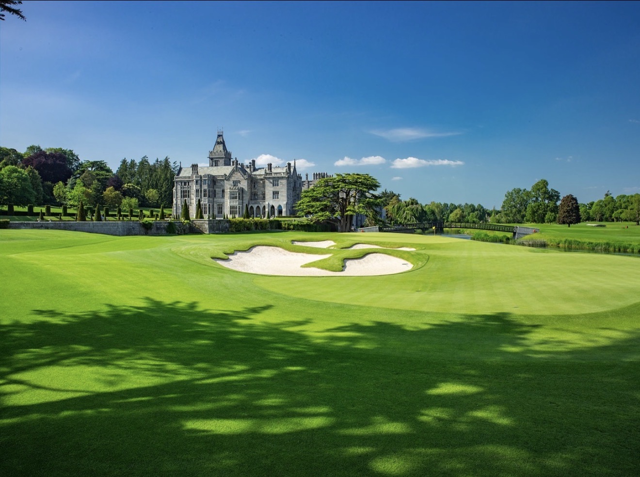 Adare Manor stone castle behind a golf green with a clover-shaped white sand bunker