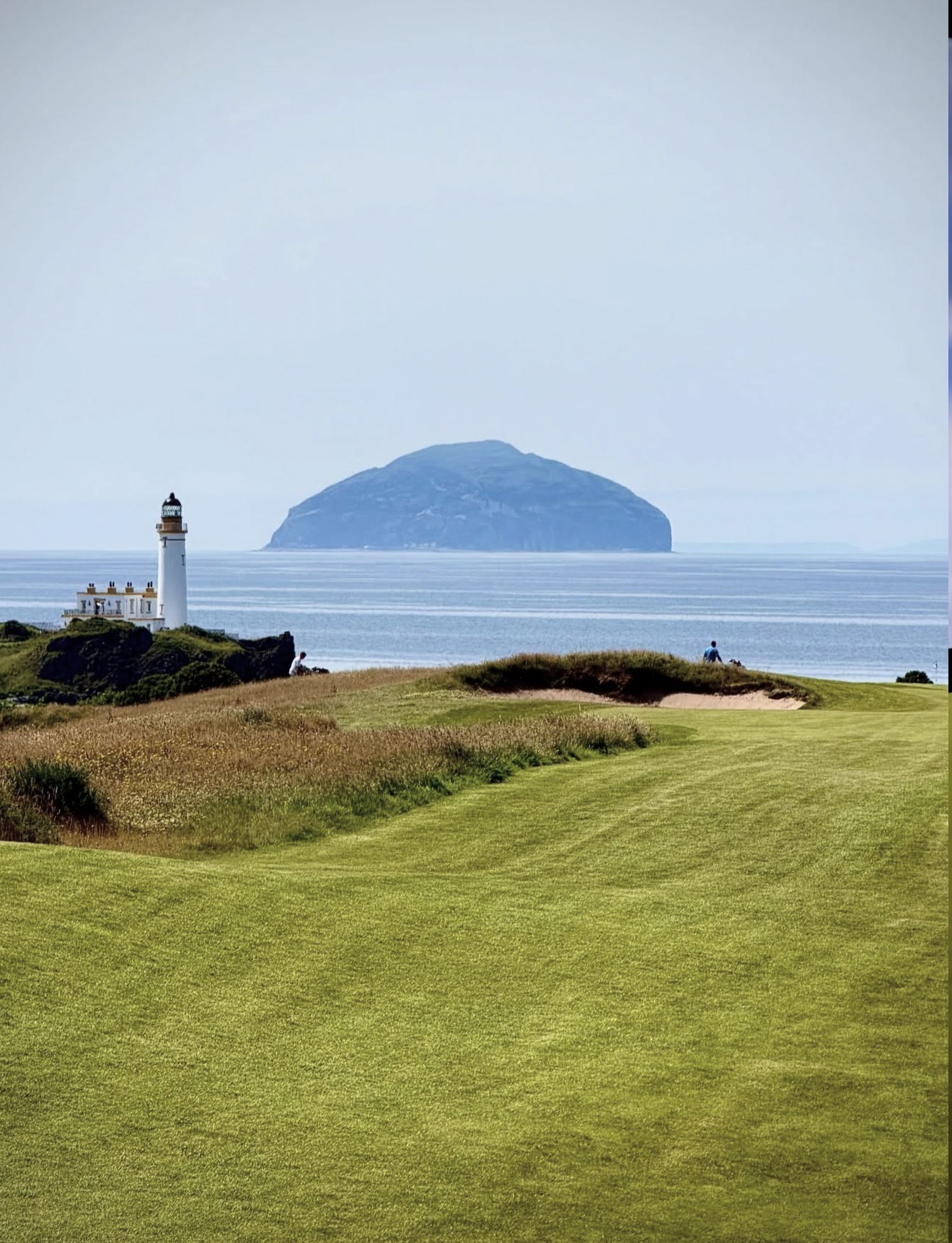 Turnberry lighthouse on the headland with Ailsa Craig rising out of the sea behind the links