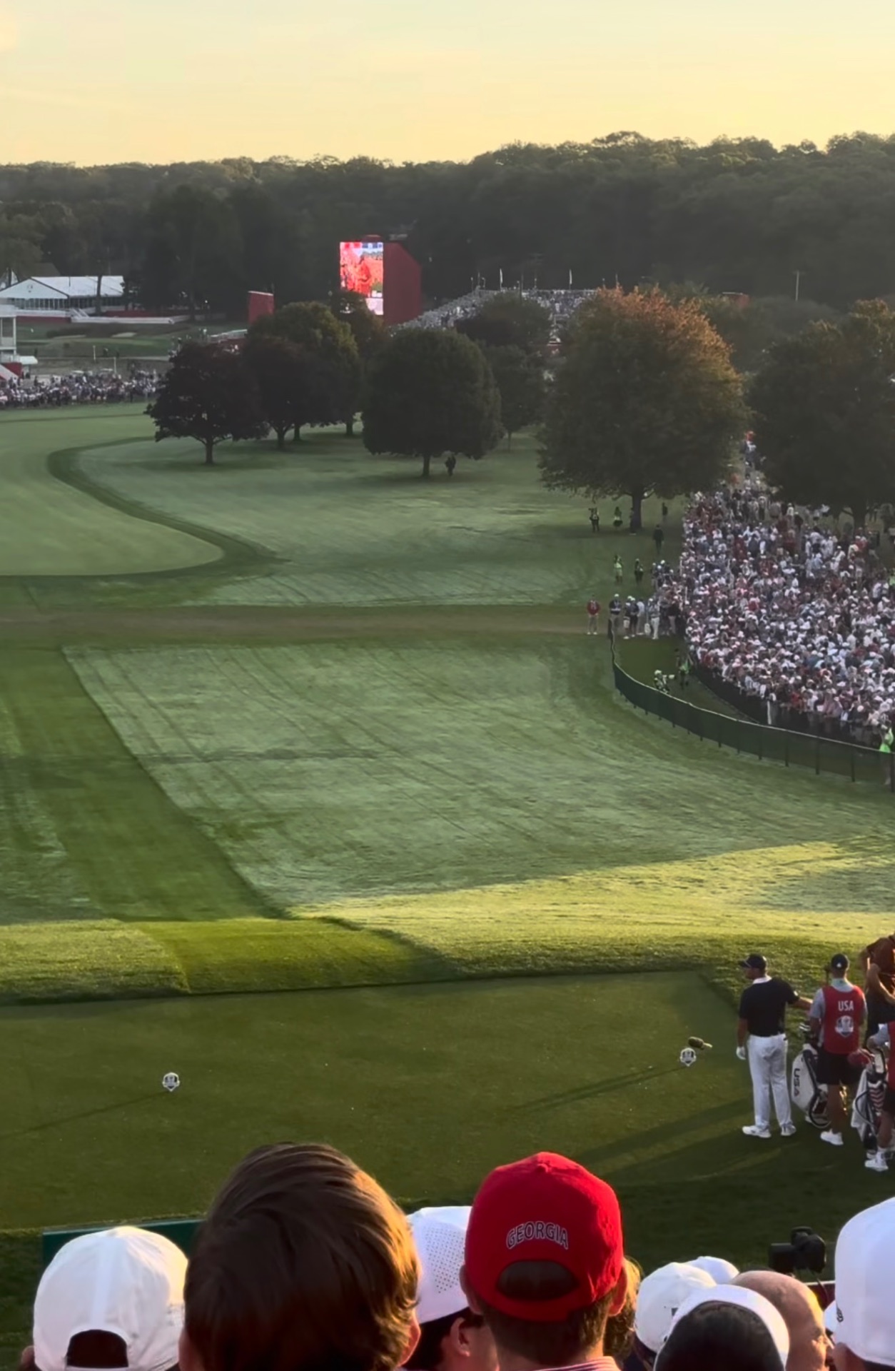 Ryder Cup 2025 tee shot at Bethpage Black with a USA caddie bag and a large tournament video board in the distance