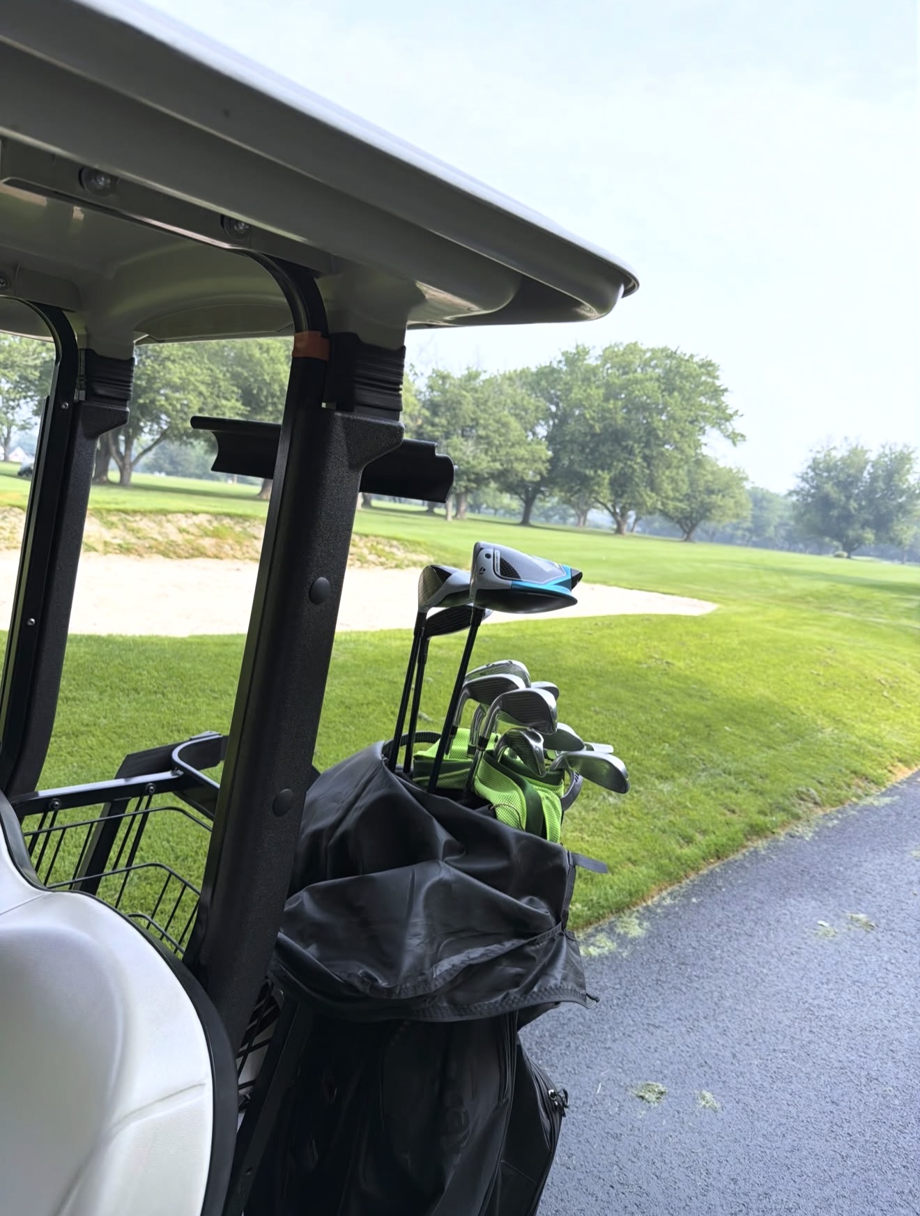 Golf cart with a club bag parked beside a parkland fairway and bunker on a summer morning